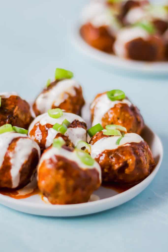 buffalo turkey meatballs on a white plate drizzled with ranch dressing and topped with green onions against a blue background