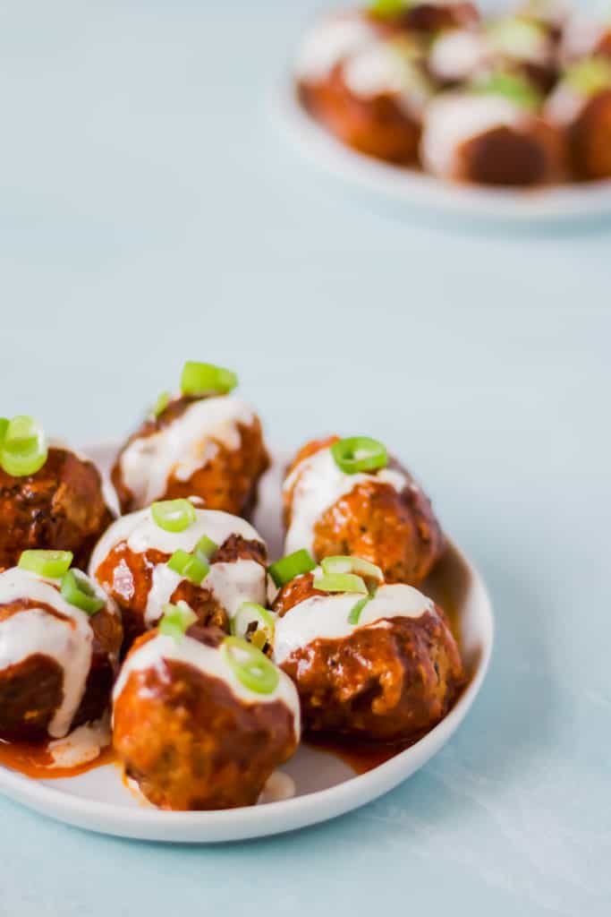  two white plates full of buffalo turkey meatballs with ranch dressing and green onions