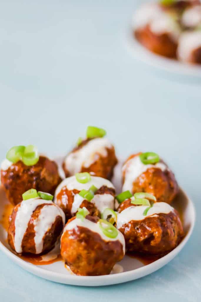 buffalo turkey meatballs on a white plate with ranch dressing and green onions against a light blue background