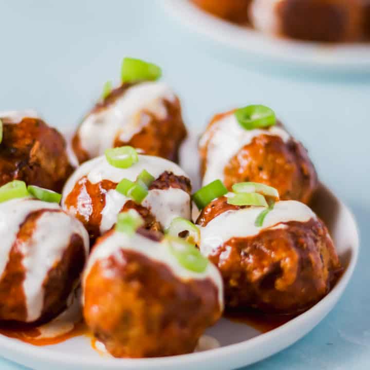 buffalo turkey meatballs on a white plate drizzled with ranch dressing and topped with green onions against a blue background