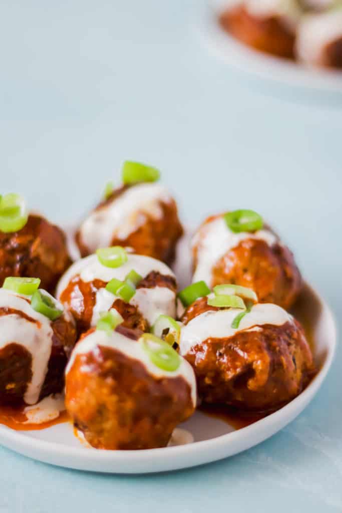 meatballs drizzled with white liquid and topped with green onions