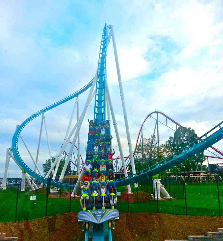 A roller coaster train filled with riders climbs a steep blue track, with twists and loops visible in the background under a cloudy sky—an energetic scene worthy of top posts at any amusement park.