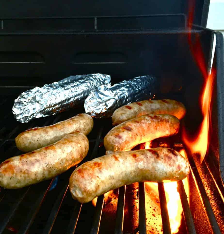 brats and corn wrapped in aluminum foil on a hot grill