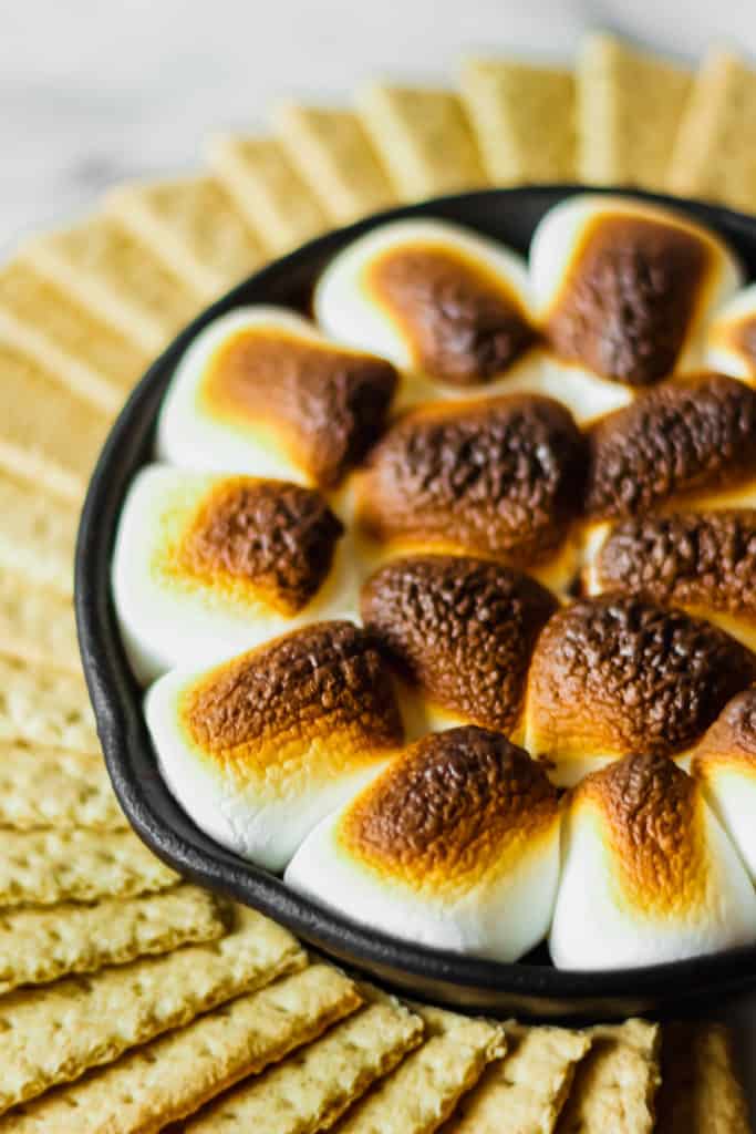 graham crackers in a circle surrounding a cast iron skillet filled with browned marshmallows