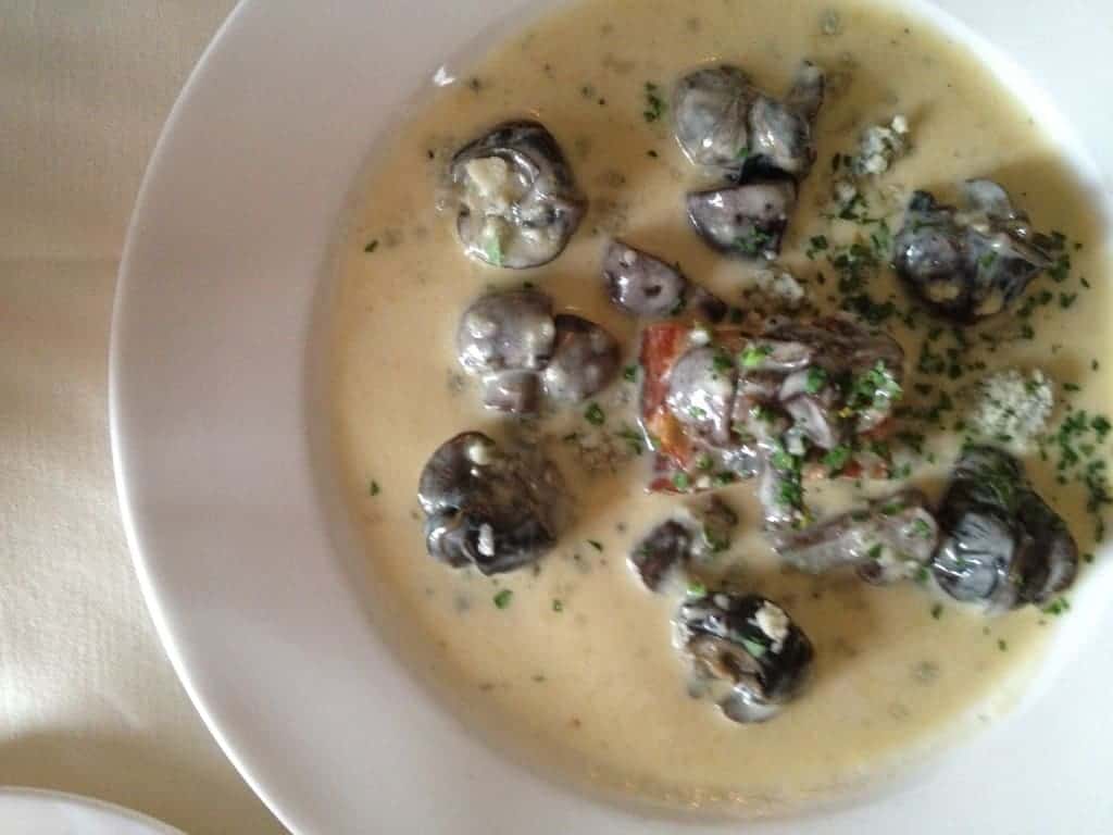 A plate of escargot in a creamy garlic sauce, garnished with chopped herbs, served on a white dish—a true highlight among Charlotte's best bites.