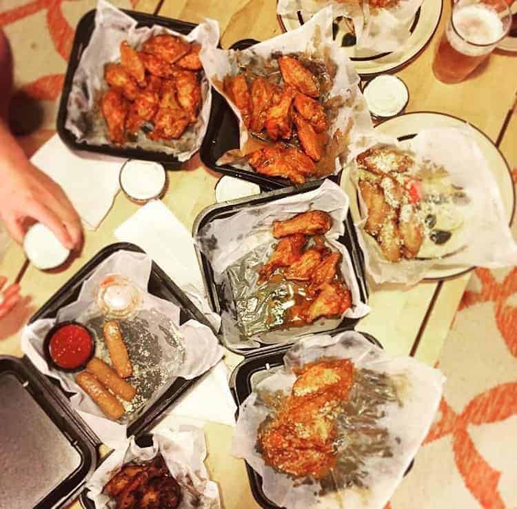 take out boxes with a variety of different hot buffalo wings on a wooden table an orange and white rug in the background