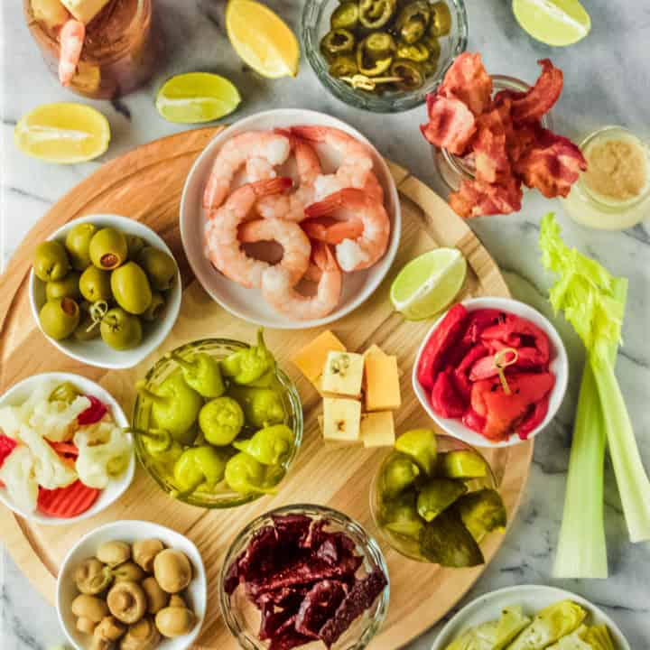 a diy bloody mary bar on a marble and wooden board with toppings and bloody mary bar ingredients