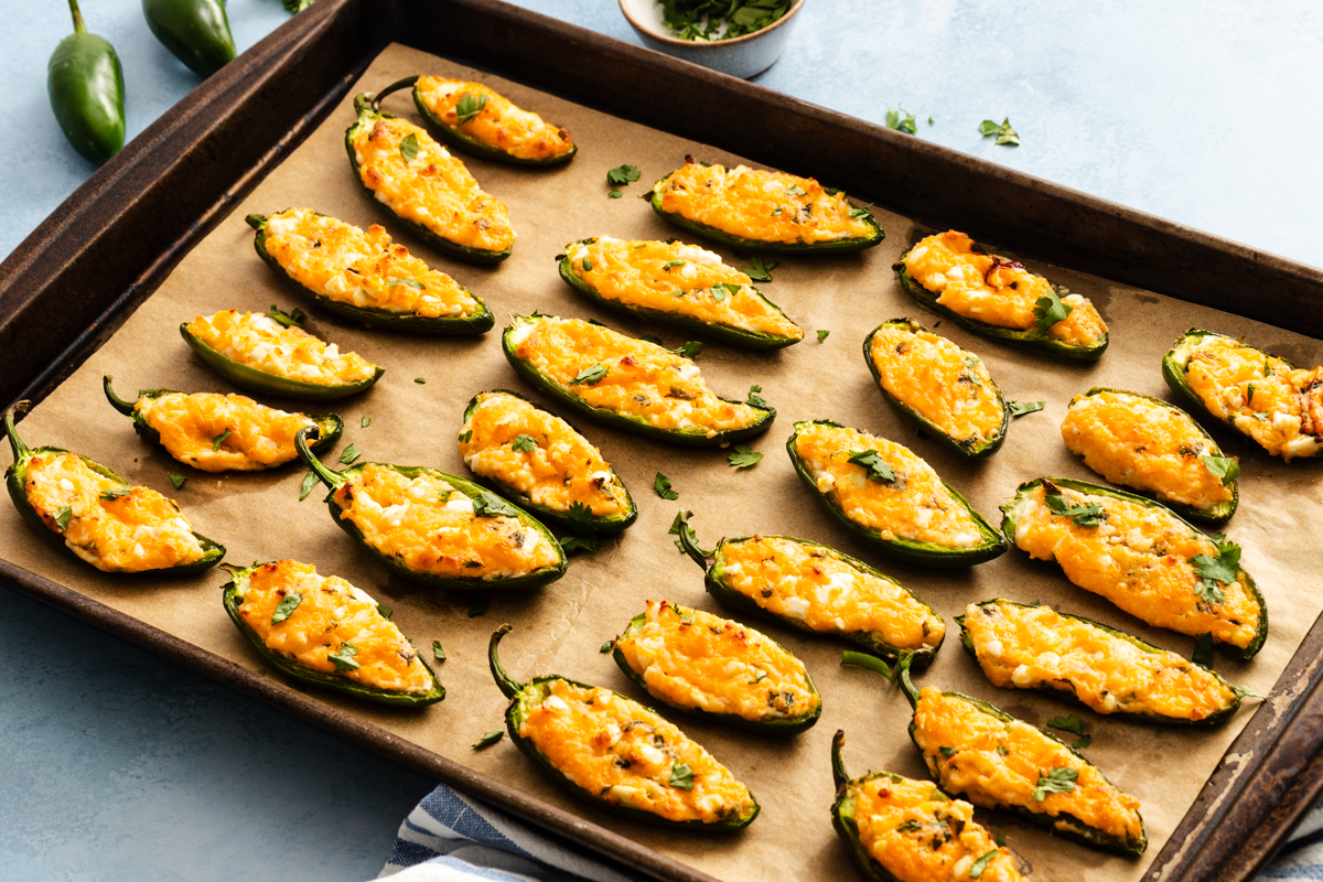Baking sheet filled with jalapeño poppers topped with melted cheese and fresh herbs.