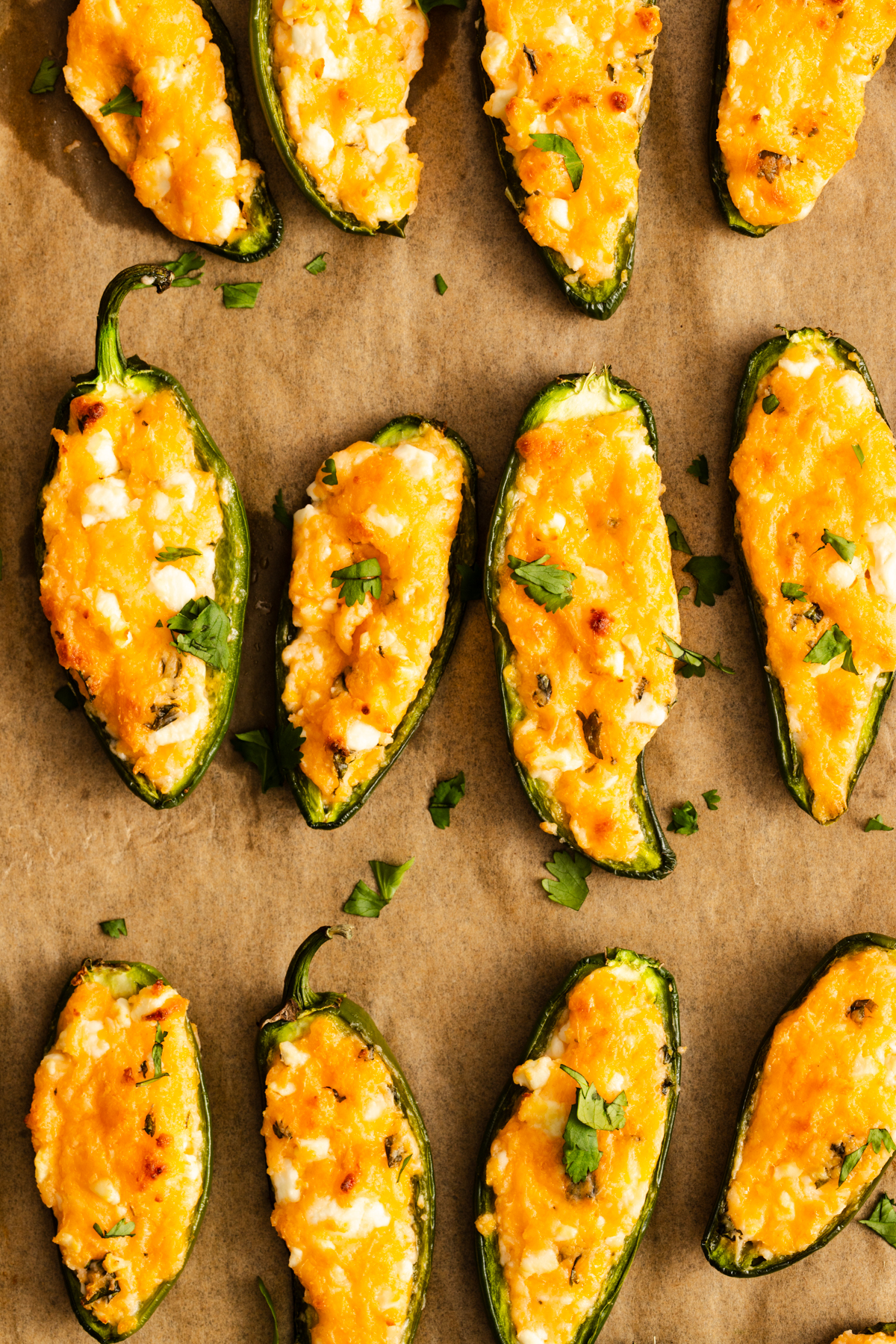 Jalapeño poppers stuffed with melted cheese and garnished with parsley on a parchment-lined baking sheet.