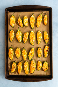 A metal baking sheet filled with rows of jalapeño poppers topped with melted cheese.