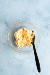A glass bowl containing pimento cheese for jalapeno poppers with a black silicone spatula.
