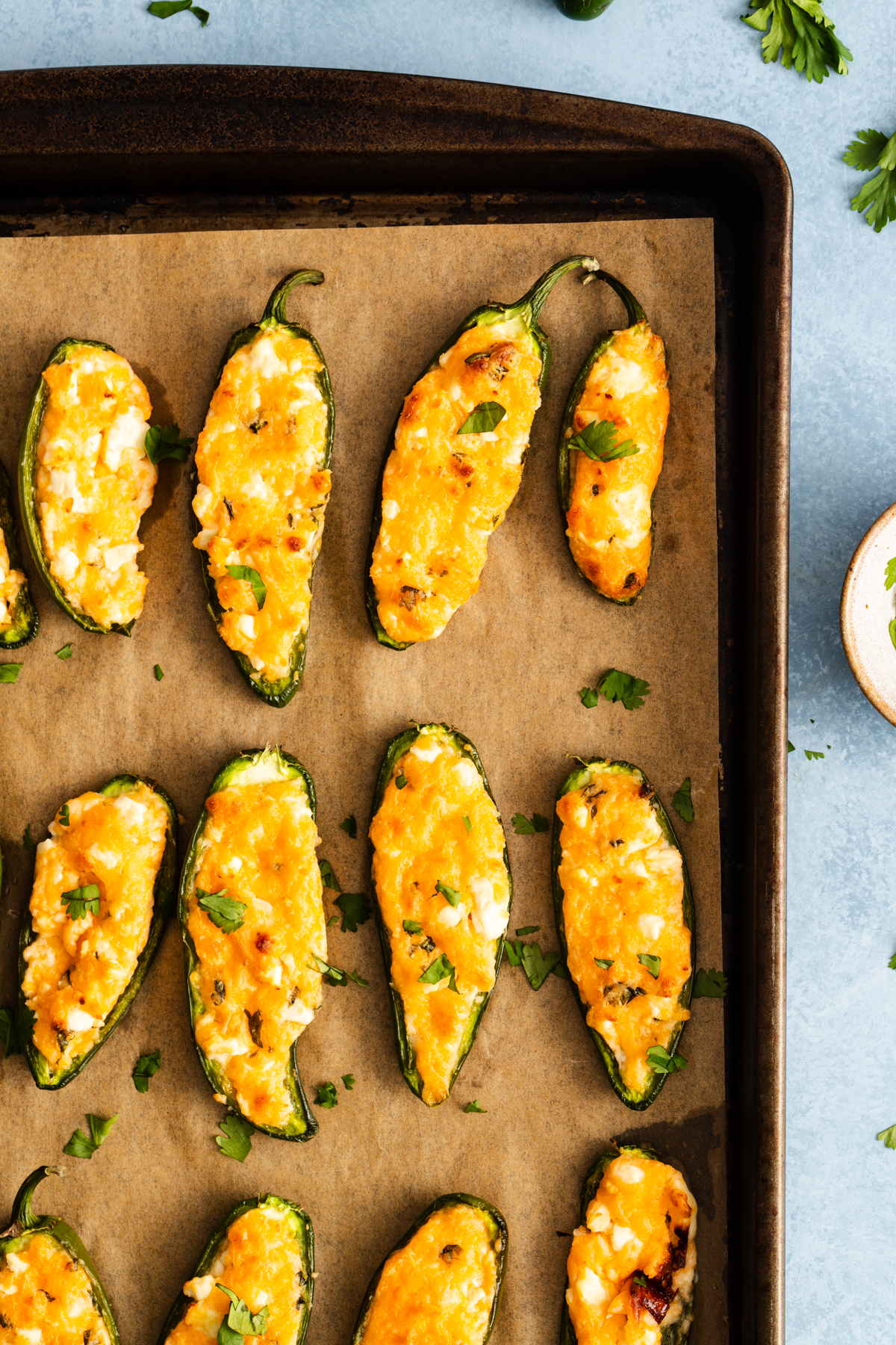 Jalapeño poppers on a parchment-lined baking sheet, filled with melted cheese and garnished with cilantro.