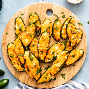 Jalapeño poppers stuffed with cheese and topped with cilantro on a round wooden serving board.