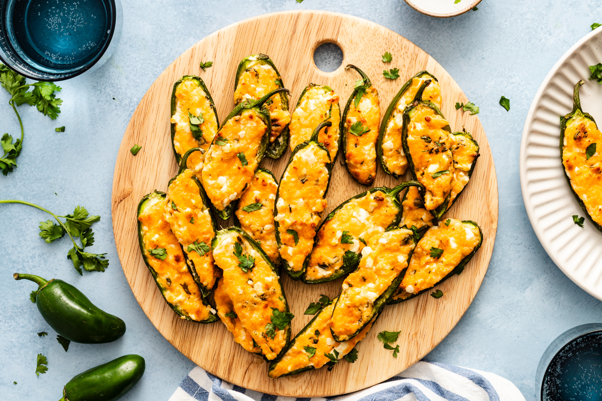 A wooden cutting board topped with cheese-stuffed jalapeño poppers garnished with cilantro.