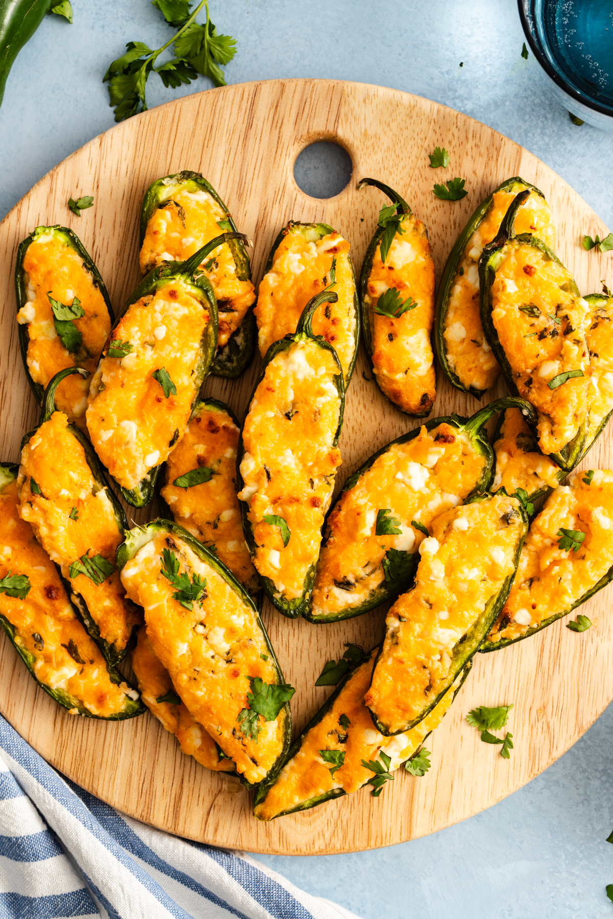 A wooden cutting board topped with multiple jalapeño poppers filled with melted cheese and garnished with fresh cilantro.