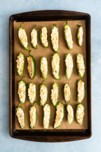 A baking sheet lined with parchment paper, filled with rows of jalapeño poppers stuffed with a creamy cheese filling.