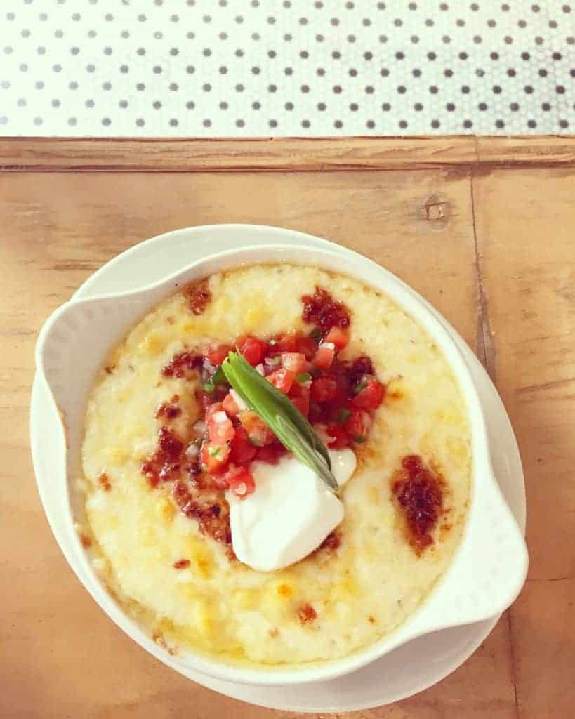 A bowl of hot, cheesy dip topped with sour cream, fresh salsa, and a green onion garnish—perfect for sharing at the best brunch in Charlotte—served on a light wooden table with a polka-dot background.
