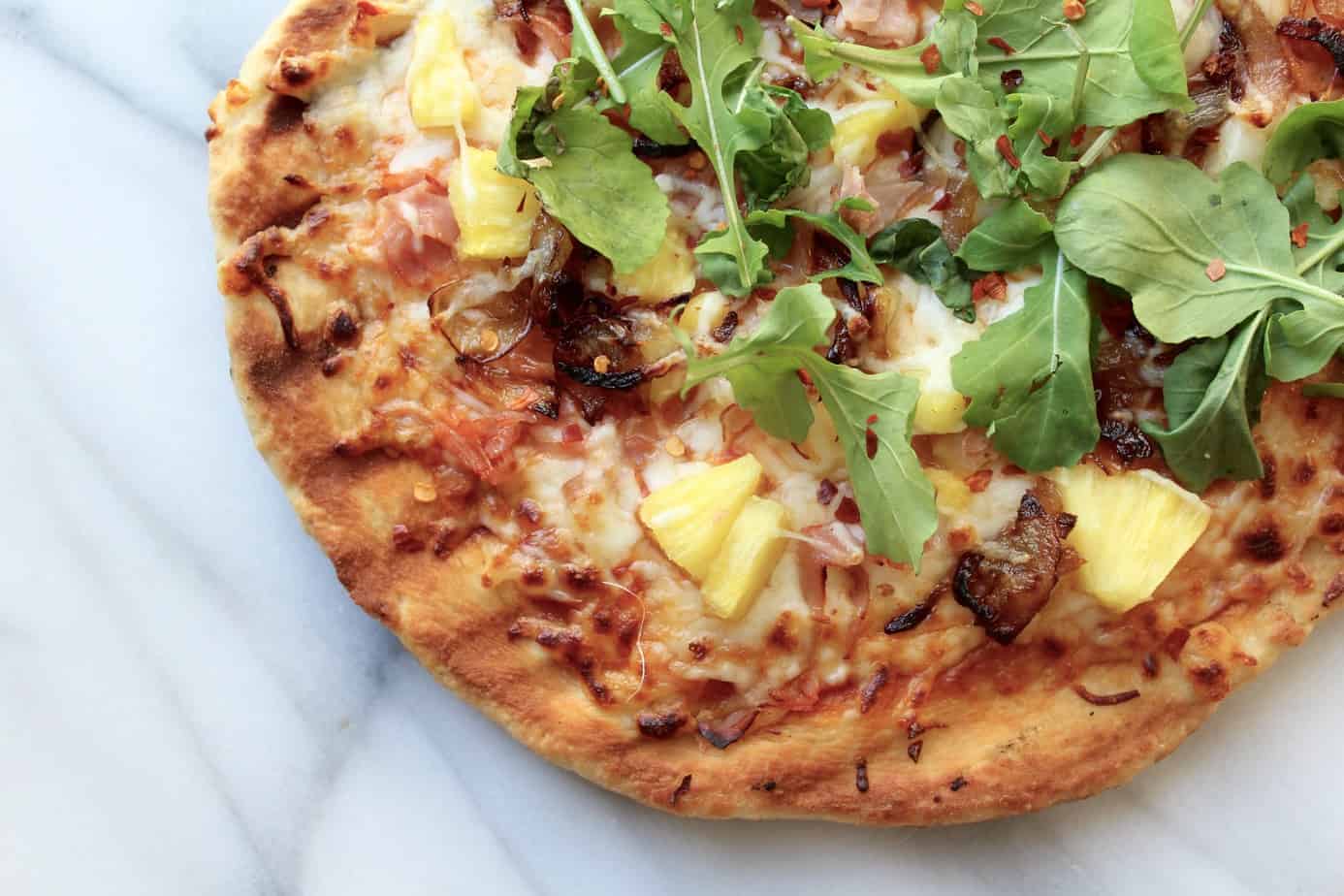 fancy hawaiian grilled pizza with ham, pineapple, caramelized onions and arugala