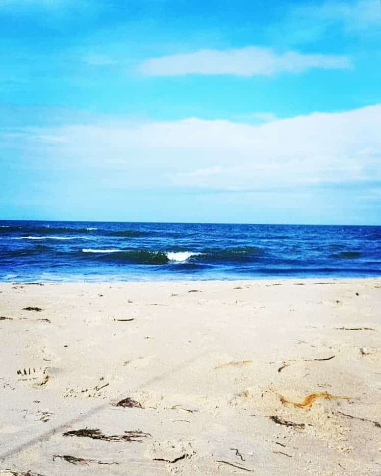 footprints in the white sand and a wave curling in the blue ocean at the outer banks