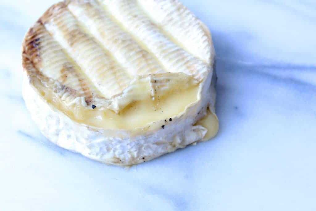 wheel of metling brie after being grilled