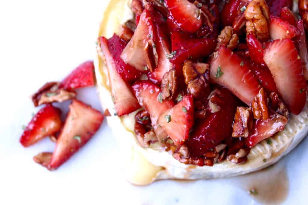 fresh strawberries on top of creamy brie on a white background