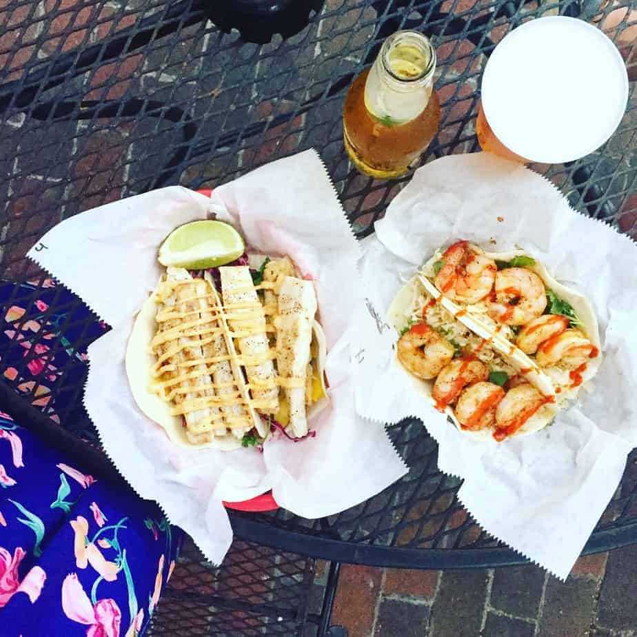two baskets filled with fish tacos and shrimp tacos on a black table with a glass of beer and bottle of beer on the side two baskets filled with fish tacos and shrimp tacos on a black table with a glass of beer and bottle of beer on the side