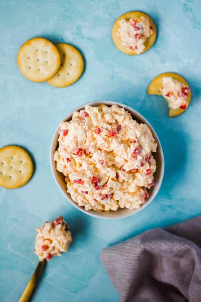 bowl of jalapeno pimento cheese on a blue background with a spoonful of cheese and crackers