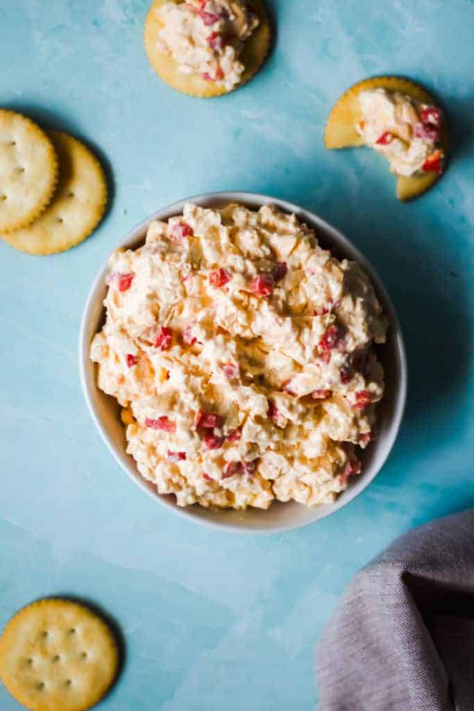 white bowl of pimento cheese with crackers on a blue background