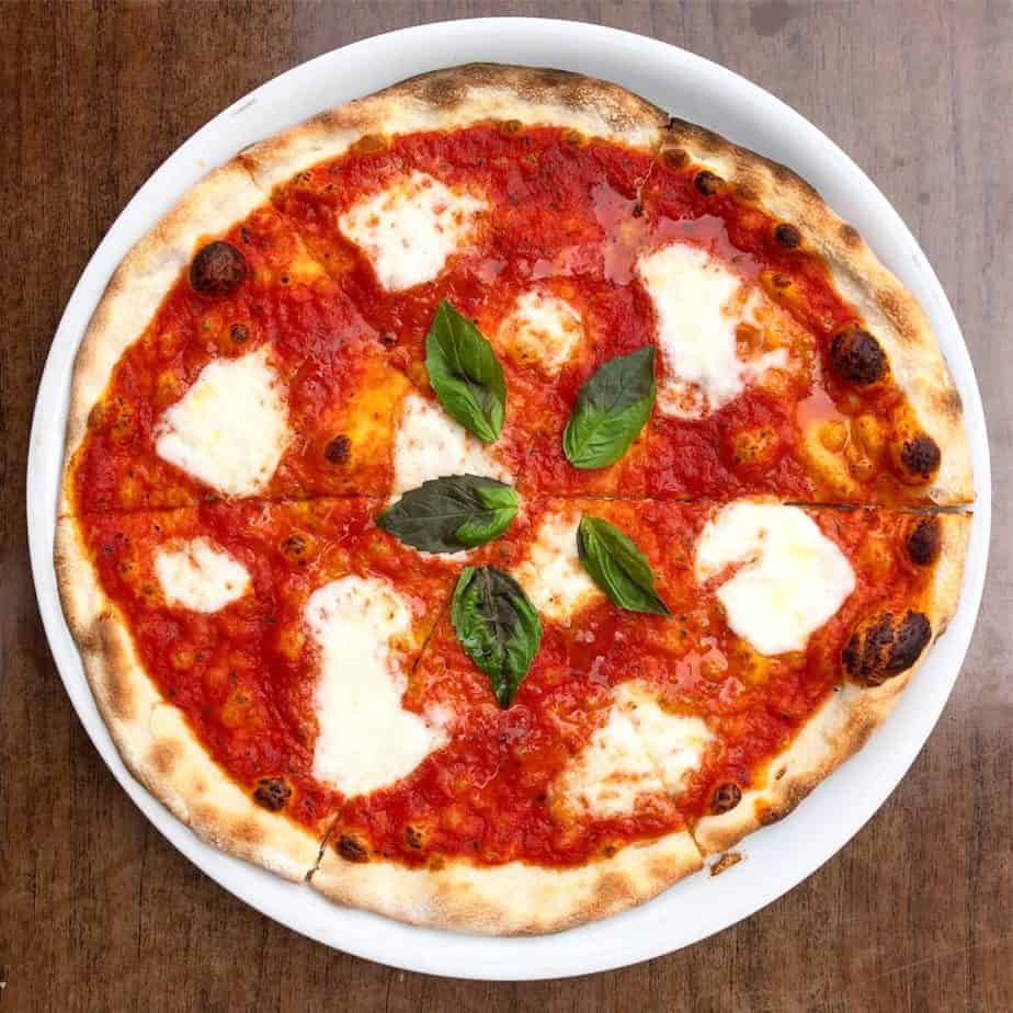 pizzeria omaggio serves some of the best pizza in charlotte. pictured is an overhead shot of pizza with red sauce and fresh mozzerlla