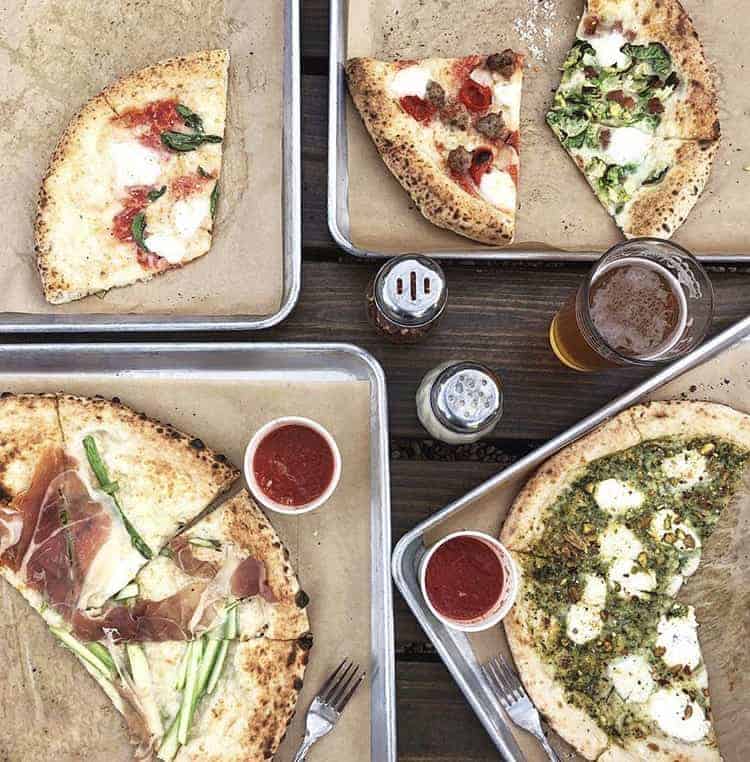 slices of pizza with red sauce, white mozzarella cheese and green toppings on metal trays 