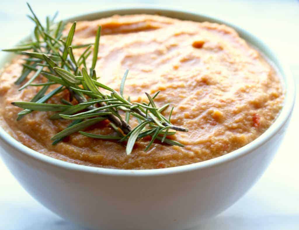 white bowl with orange paleo butternut squash soup garnished with a sprig of fresh, green rosemary