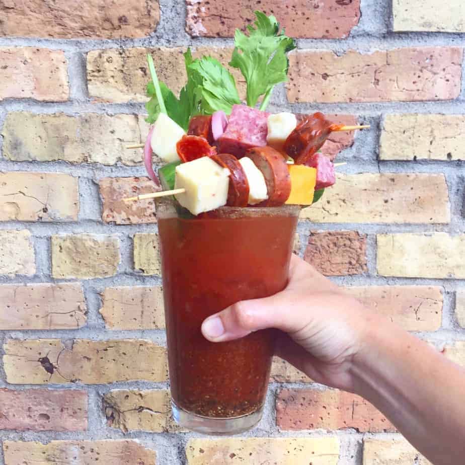 bloody mary with cheese sausage celery vegetables in front of a brick wall