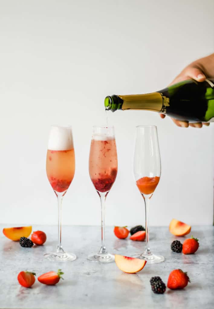 pouring champagne into a flute filled with fruit puree to make strawberry bellinis