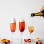 three champagne flutes filled with fruit puree and champange on a marble background with fruit