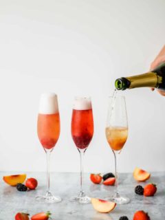 three champagne flutes filled with fruit puree and champange on a marble background with fruit