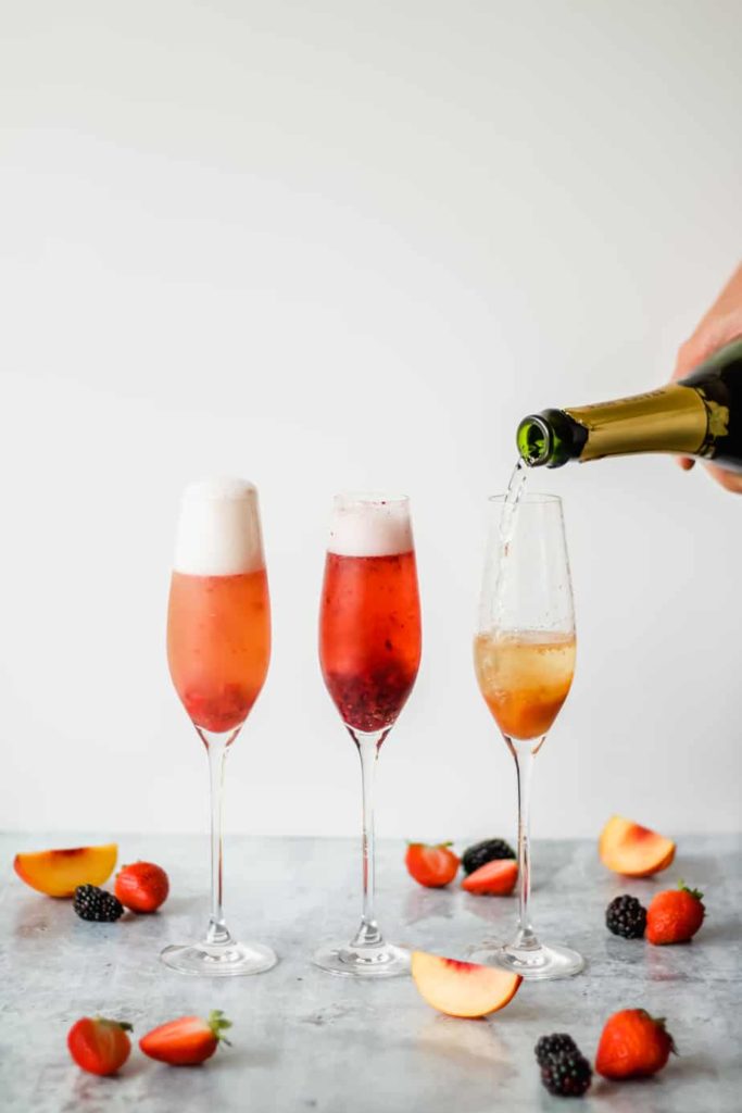 three champagne flutes filled with fruit puree and champange on a marble background with fruit