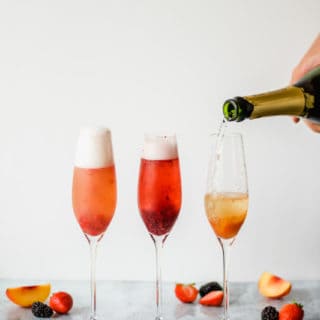 three champagne flutes filled with fruit puree and champange on a marble background with fruit