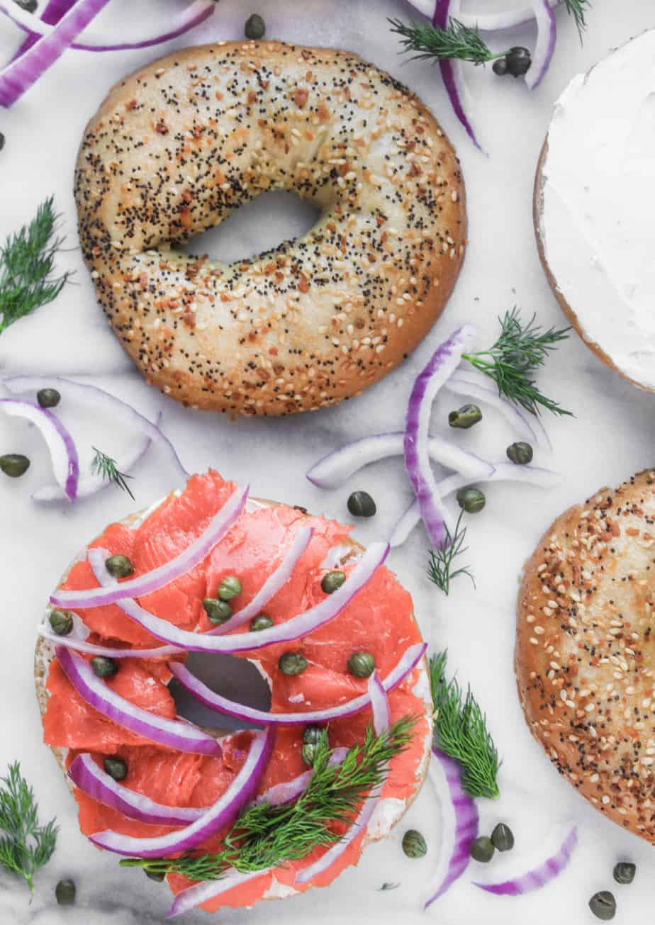 four halves of everything bagels, one topped with smoked salmon and red onion and one topped with plain cream cheese