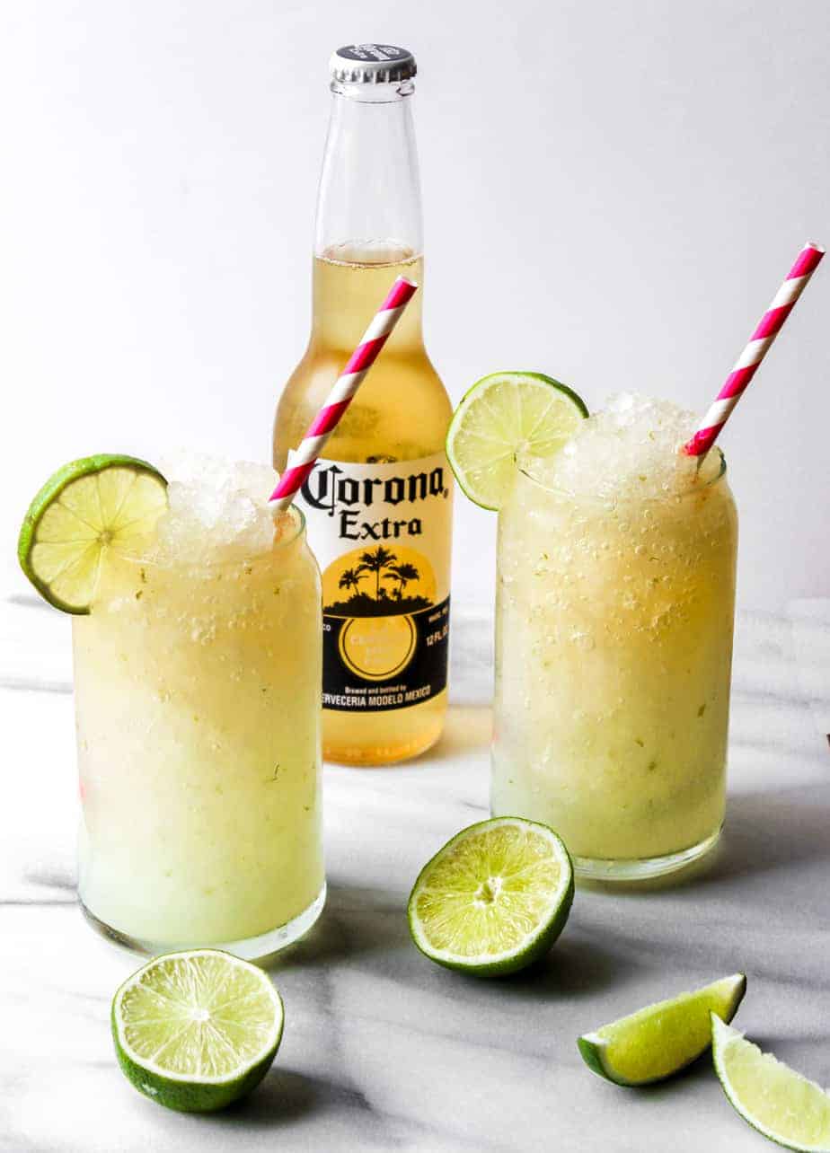 bottle of corona with two corona cocktails, limes and pink straws