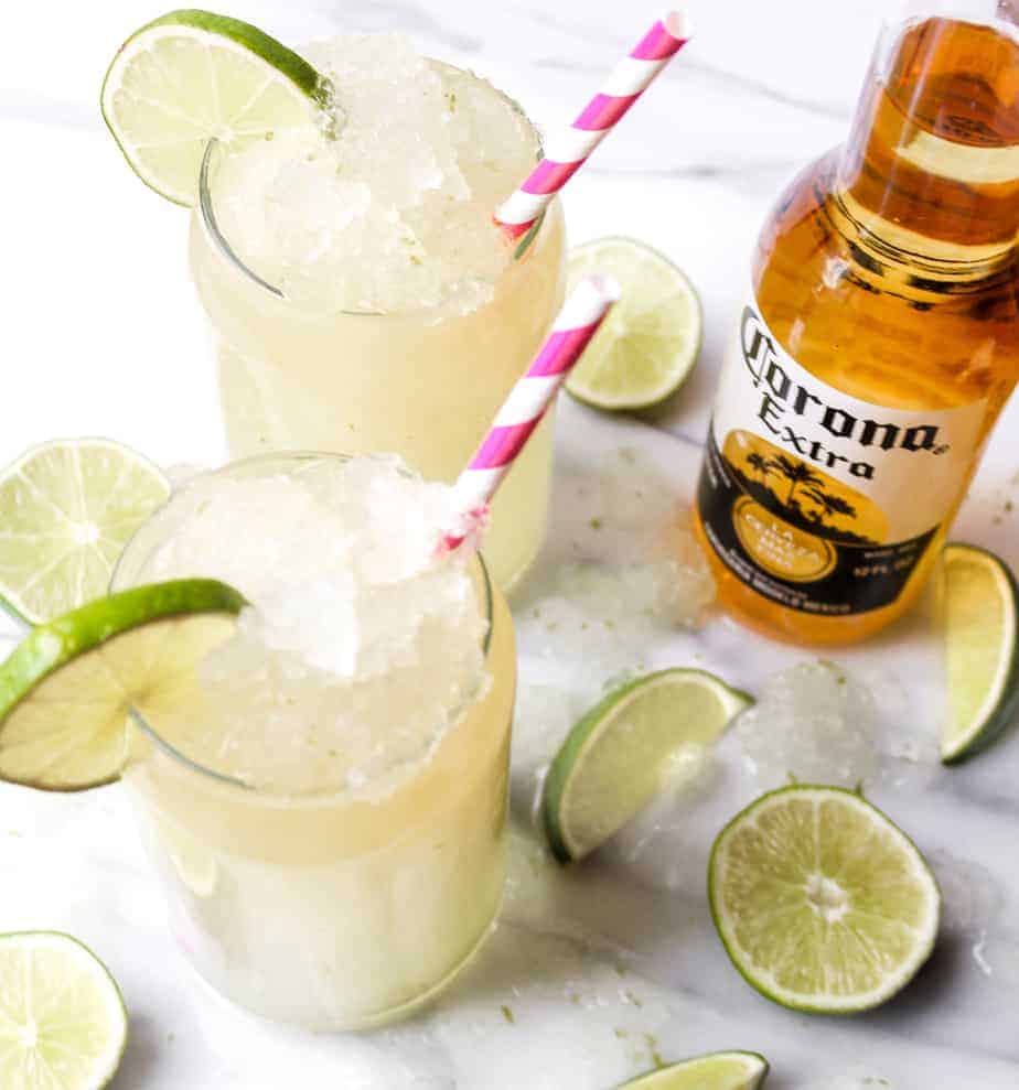 bottle of corona extra with two corona cocktails in glasses with ice and lime