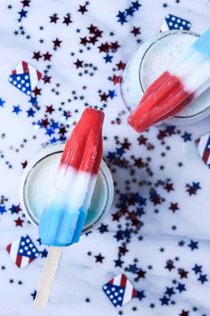 two red white and blue popsicles on top of two cups surrounded by american flag confetti