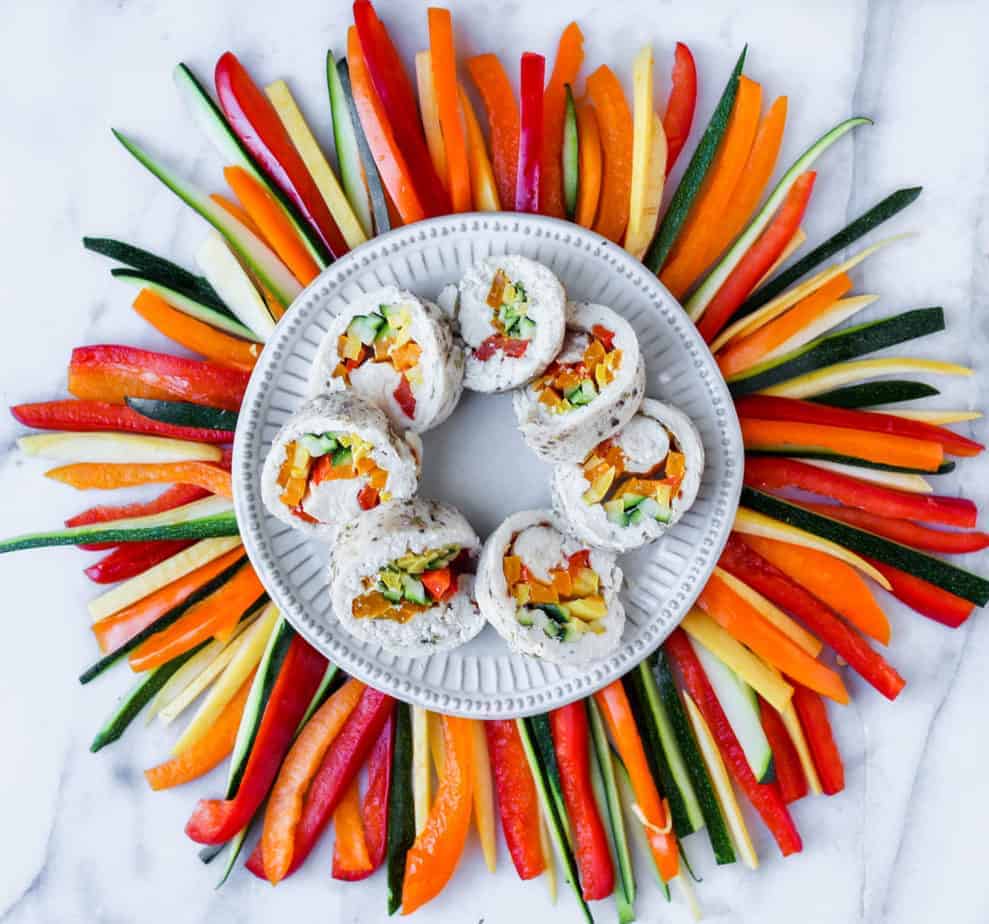 poached chicken stuffed with seasonal vegetables sliced and arranged on a white plate surrounded by a fan of mulitcolored peppers and zucchini