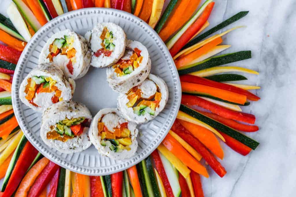 white plate with slices of chicken and seasonal vegetables surrounded by colorful peppers and squash