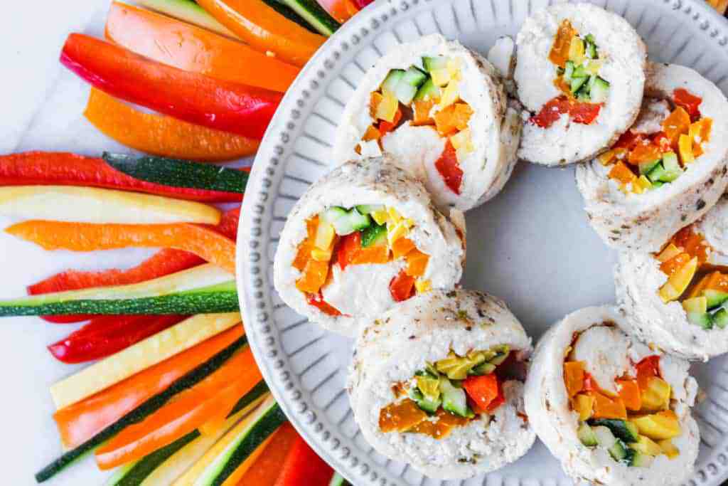 poached chicken with vegetables on a white plate with colorful vegetables in the background