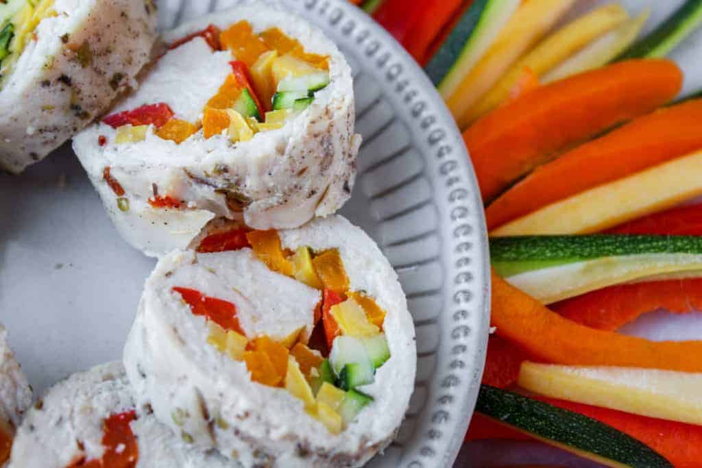 poached chicken stuffed with red, orange yellow and green summer vegetables on a white plate