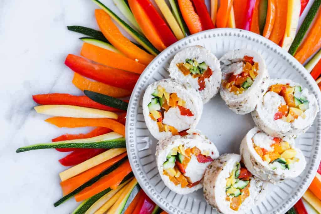 poached chicken with vegetables sliced and served on a white plate with red, orange, yellow and green vegetables surrounding it