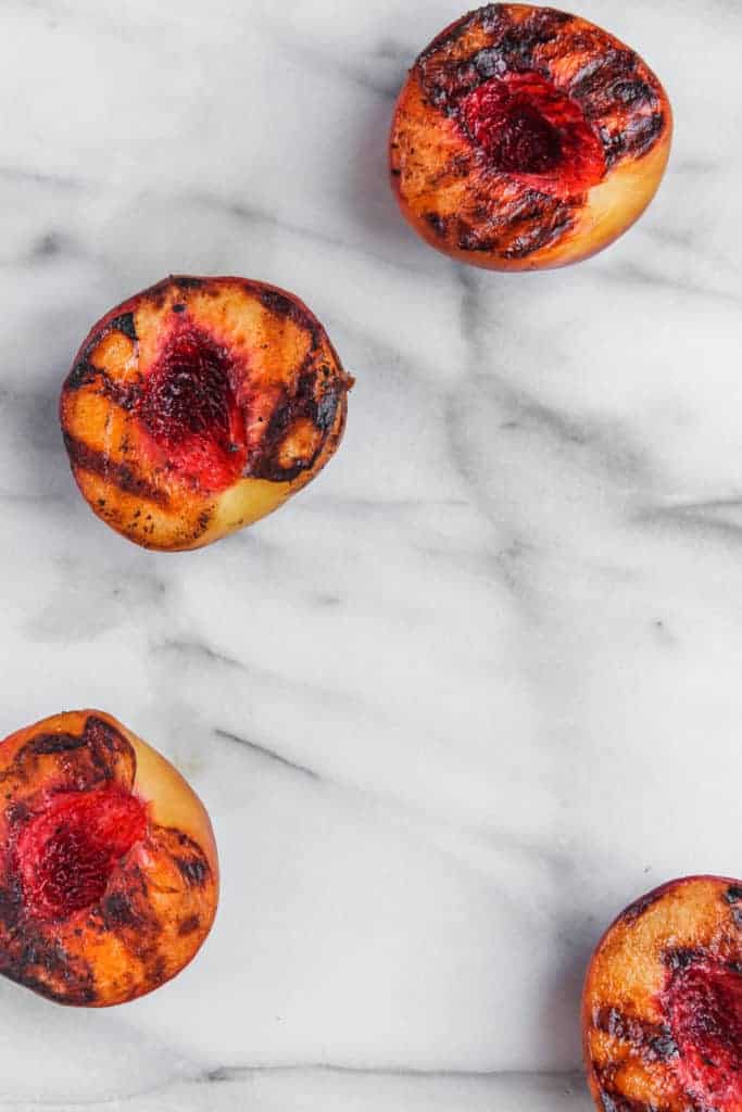 four grilled peach halves on a marble background