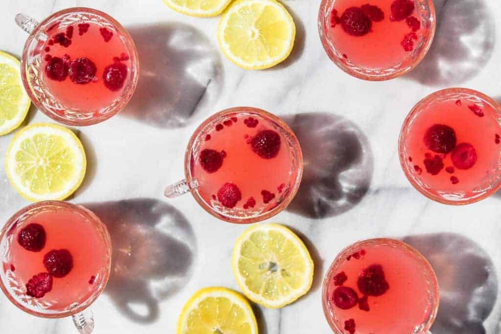 six cups of baby shower punch in glass cups with lemon slices on a marble board