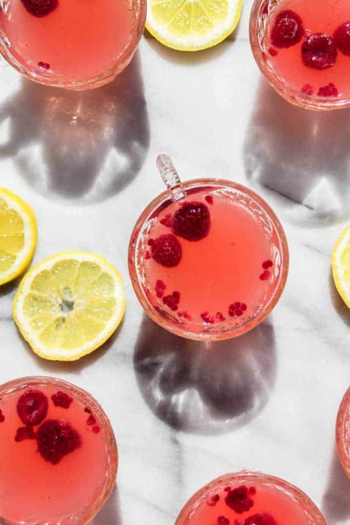 two raspberries floating in a small glass of sparkling raspberry lemonade punch with slices of lemon