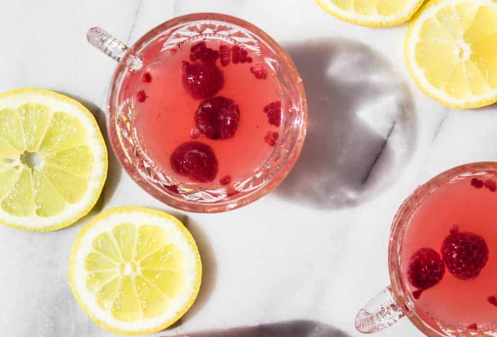 two glass cups with handles filled sparkling raspberry lemonade punch with lemons